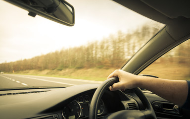 Male driver hands on steering wheel of a car and road