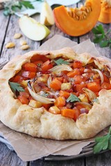 Pumpkin-apple galette with onion and bacon on a wooden table