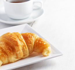Cup of coffee and croissant on white wooden table