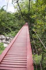 Red wooden suspension bridge over the stream, Thailand