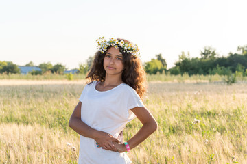 Fototapeta na wymiar Teen girl with a wreath of daisies in field