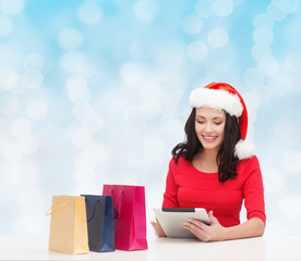 smiling woman in santa hat with bags and tablet pc