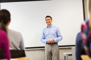 group of students and smiling teacher in classroom