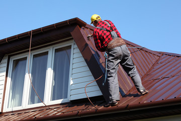 roofer builder worker spraying paint on metal sheet roof - 70930454