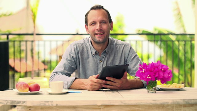 Happy, cheerful man with tablet computer sitting by the table on