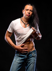 Young handsome man in a white wet T-shirt on a dark background