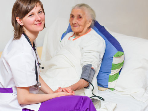 young nurse caregiving an old lady lying in bed
