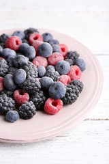 Iced berries on plate, on color wooden background