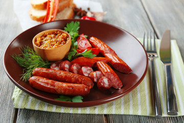Assortment of tasty thin sausages on plate on wooden background