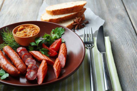 Assortment of tasty thin sausages on plate on wooden background