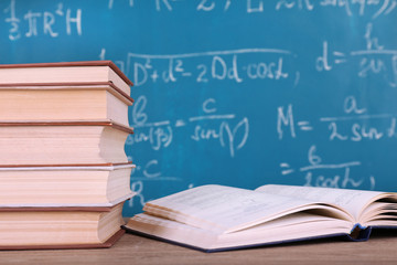 Books on wooden table on blackboard background
