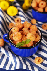 Yellow raspberries in dark blue mugs and wildflowers