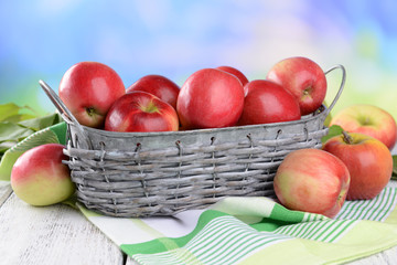 Sweet apples in wicker basket on table on bright background