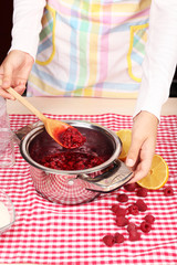 Woman cooking raspberry jam in kitchen