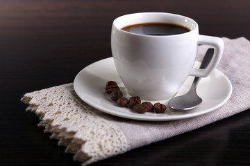Cup of coffee and coffee beans on napkin on dark background