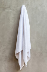Fototapeta premium Hanging white towel draped on exposed concrete wall in the bathr