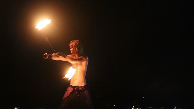 Male Artist of the spins fire poi on a rock