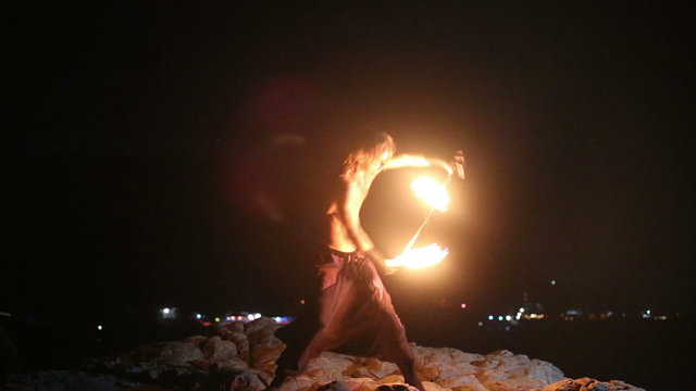 Male Artist of the spins fire poi on a rock