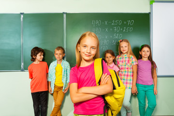 Girl wears bag and stands near the blackboard