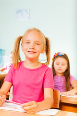 Smiling pupil holds pencil and sits at desk