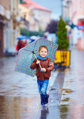 cute kid, boy walking in puddle in rainy city
