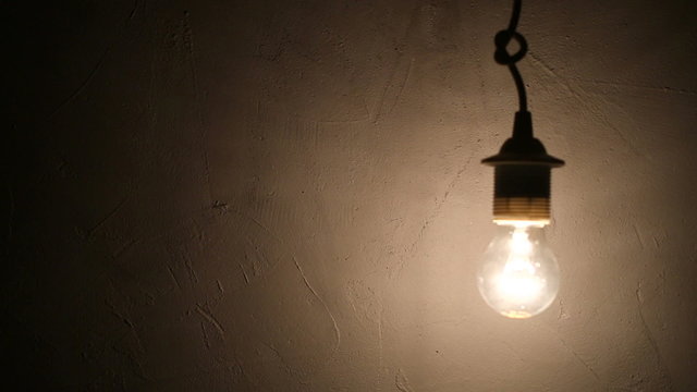 lightbulb flickers against a grunge concrete wall