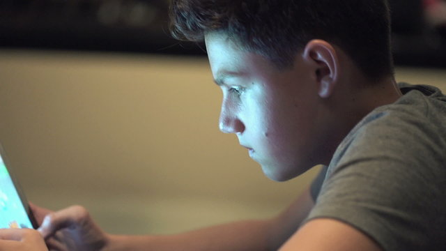 Young teenager playing game on tablet computer at night