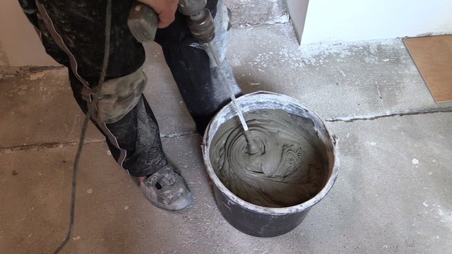worker mix adhesive cement for tile on bucket with tool