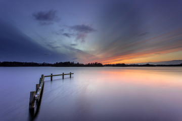 Fototapeta na wymiar Winter Sunset over Tranquil Lake with Wooden Mooring Post