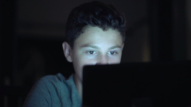 Young teenager playing game on tablet computer at night