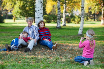 Fototapeta premium Young pretty girl photographing her family by phone in park