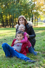 Naklejka na ściany i meble Grandmother with two grandchildren sit on green grass in park