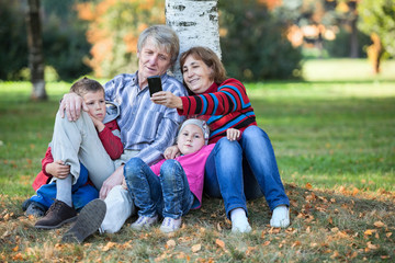 Naklejka na ściany i meble Grandparents with children sit together and make selfie phone