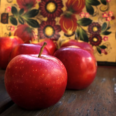 Red apples on wooden surface and floral painting background