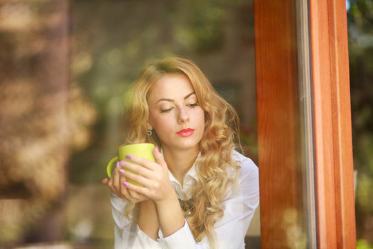 Pensive woman drinking coffee at home, looking out the window - Powered by Adobe