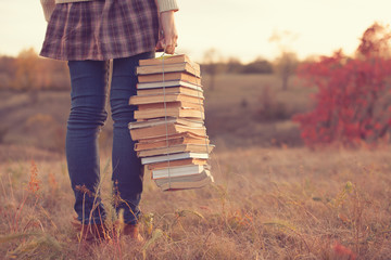 Hipster girl holding a stack of books - obrazy, fototapety, plakaty