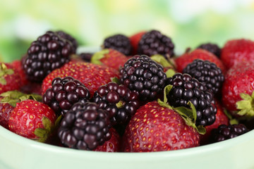 Strawberries and blackberries in bowl on bright background