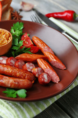 Assortment of tasty thin sausages on plate on wooden background