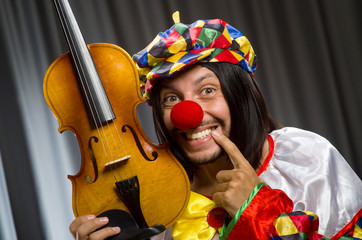 Funny clown plyaing violin against curtain