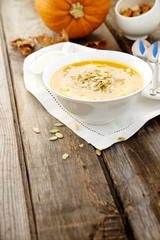 Pumpkin soup in a white cup on wooden background