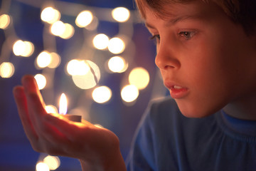 boy holds in a hand a burning candle against sparks