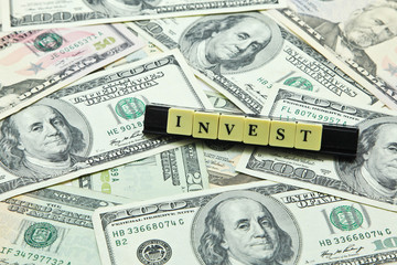 Fototapeta premium Word invest on pile of US dollar banknotes