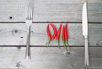 Spicy meal concept with chilis, knife and fork over a wooden bac