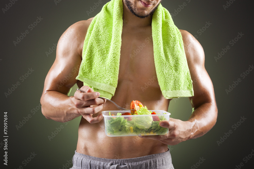 Wall mural fitness man holding a bowl of fresh salad on black background