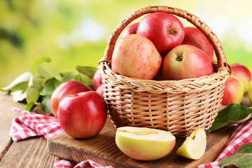 Sweet apples in wicker basket on table on bright background
