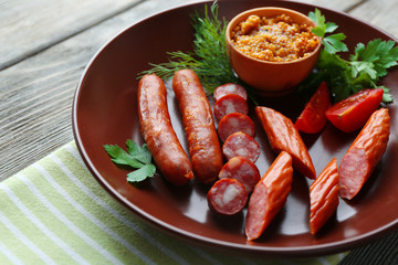 Assortment of tasty thin sausages on plate on wooden background