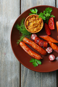 Assortment of tasty thin sausages on plate on wooden background