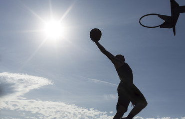 Basketball player silhouette slam dunking on a sunny day