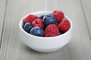 raspberries and blueberries in white bowl