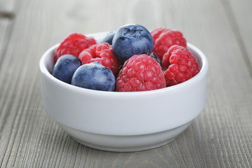 raspberries and blueberries in white bowl